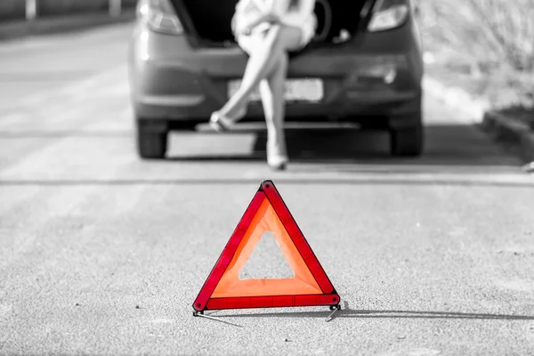 Woman sitting on broken car near red warning sign — Stock Photo, Image