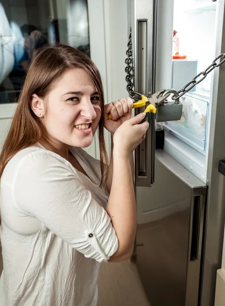 Angry woman cutting chain on refrigerator with cutters — Stock Photo, Image