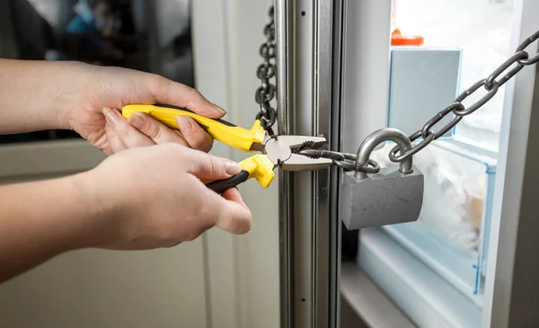 Foto de mulher tentando cortar corrente na geladeira com alicate — Fotografia de Stock