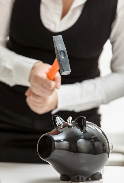 Photo of woman smashing black piggy bank with hammer