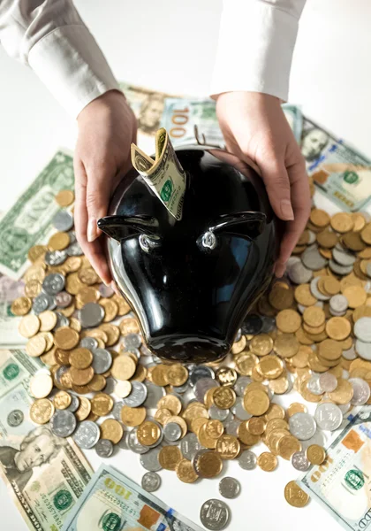 Foto de la mujer sosteniendo caja de dinero de cerdo negro en la pila de monedas — Foto de Stock