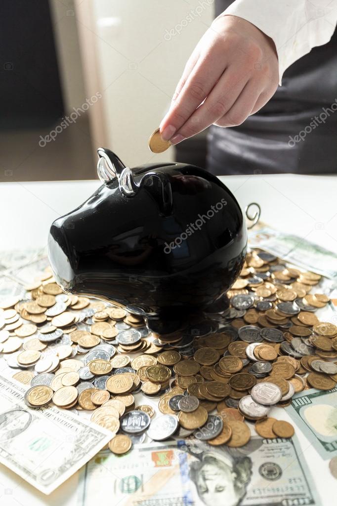 businesswoman putting coin in black piggy bank
