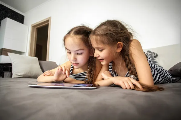 Portrait of two sisters lying on bed with tablet — Stock Photo, Image