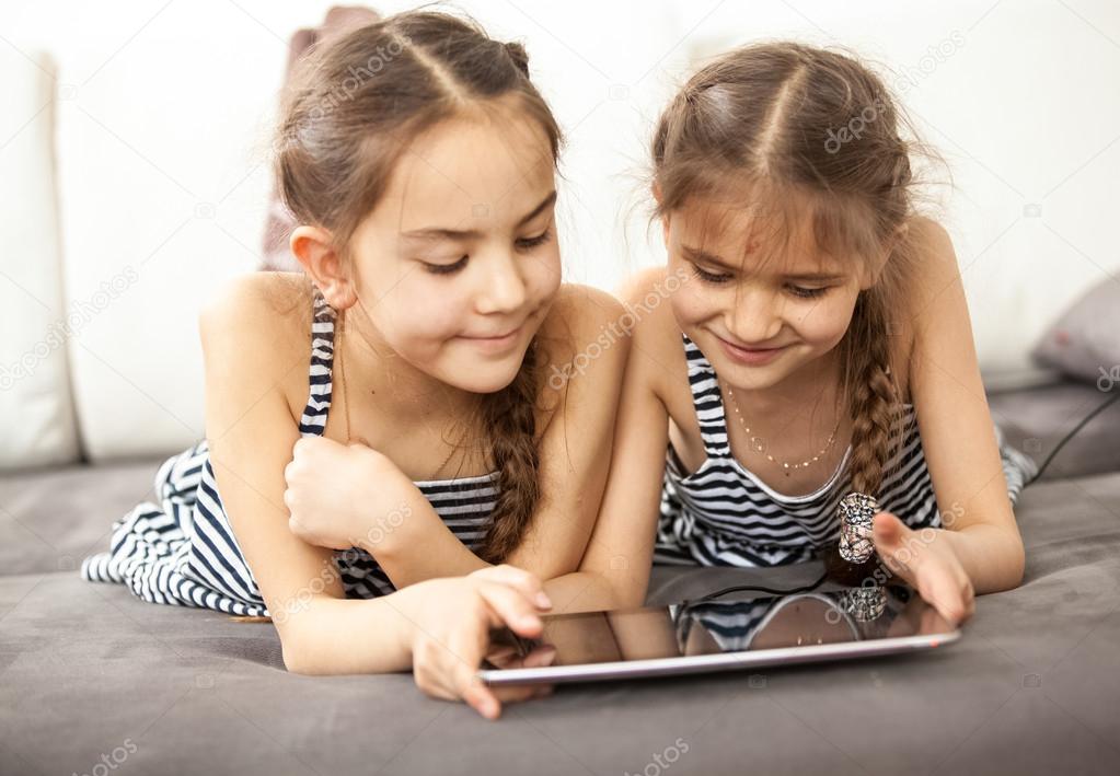 smiling schoolgirls lying on couch and playing on tablet
