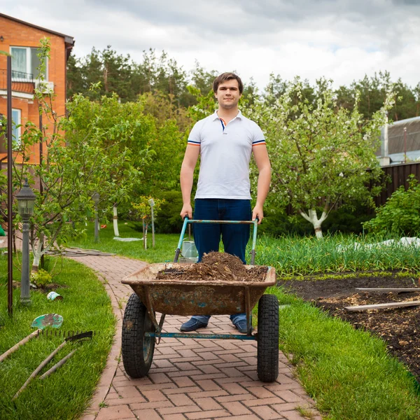 Junger Mann trägt Gartenschubkarre — Stockfoto
