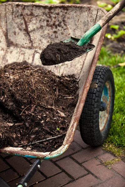 Photo of spade putting soil in old wheelbarrow — Stock Photo, Image