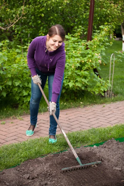 Schöne Frau arbeitet mit Harke auf Gartenbeet — Stockfoto