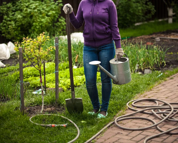 Mujer sosteniendo pala y regadera en el jardín — Foto de Stock