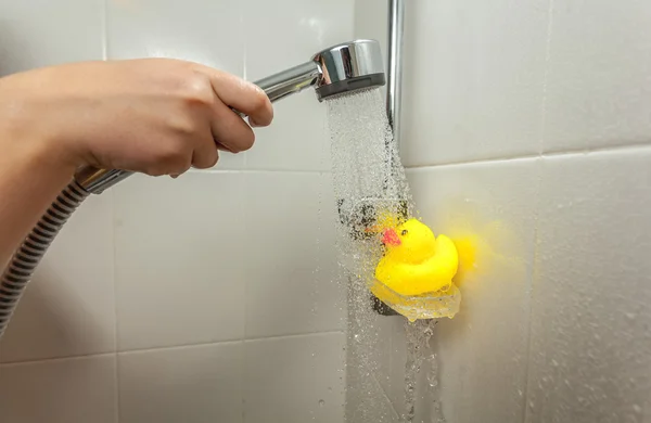 Фото мужчины, держащего ручной душ над резиновой уткой — стоковое фото
