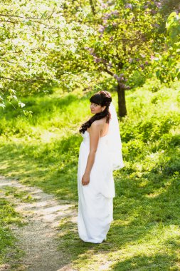 parkta ağaçların altında yolda yürüyen esmer gelin