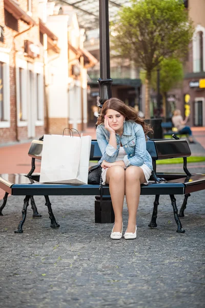 Sad woman sitting on bench with shopping paper bag — Stock Photo, Image