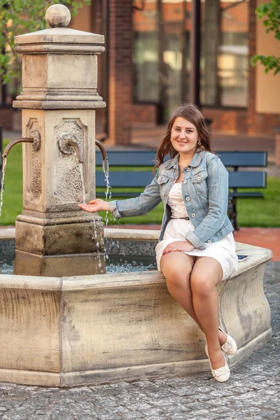 Mujer sonriente sentada al lado de la fuente en la ciudad vieja —  Fotos de Stock