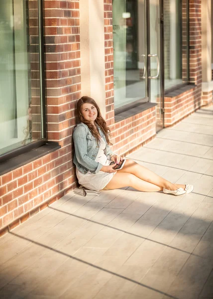 Kadın sokakta oturan ve tuğla duvara yaslanmış — Stok fotoğraf