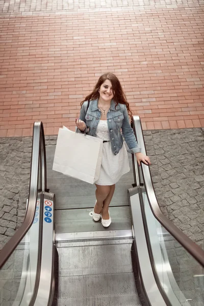 Woman with paper bag going on escalator at shopping mall — Stock Photo, Image