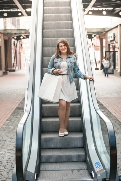 Femme marche sur l'escalator tenant sac en papier blanc — Photo