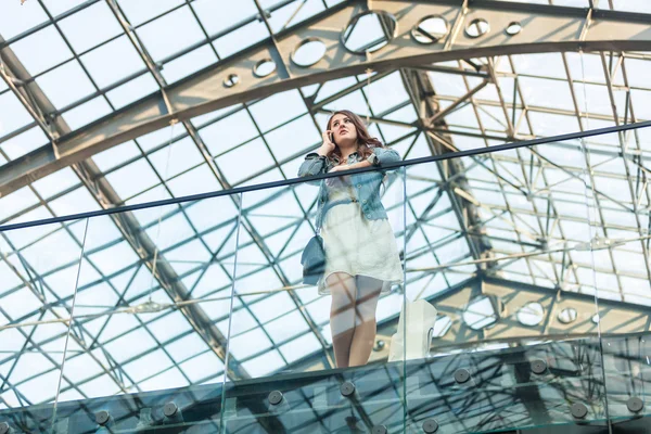 Женщина разговаривает по мобильному телефону в аэропорту со стеклянным потолком — стоковое фото