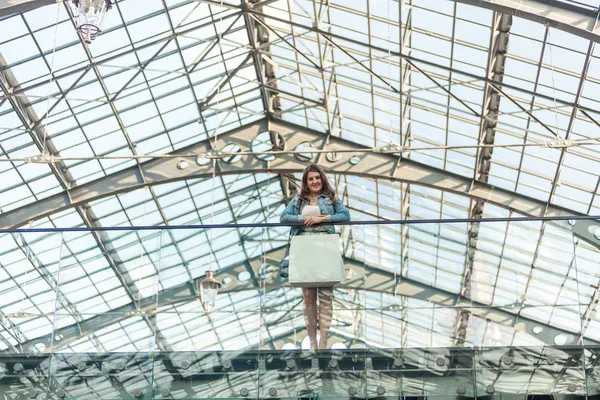 Mujer con bolsa de papel blanco de pie en el centro comercial con techo de cristal — Foto de Stock