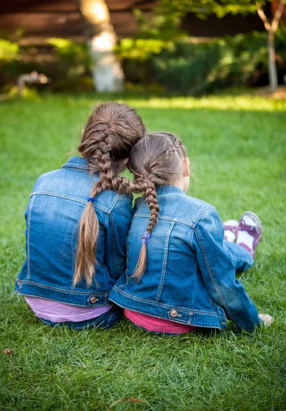 Little sisters sitting on grass head to head with joint braids — Stock Photo, Image
