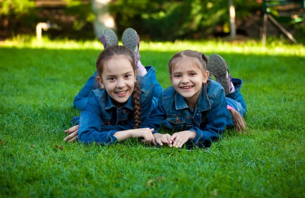 Uśmiechnięte dziewczyny za pomocą tabletu, leżąc na trawie w ogrodzie — Zdjęcie stockowe