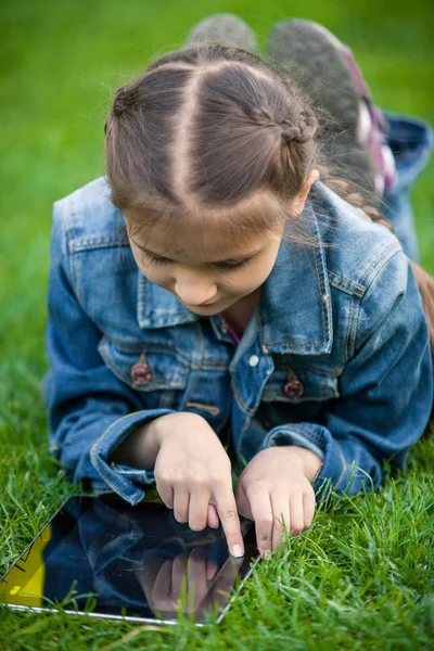 Menina deitada na grama e apontando para touchscreen — Fotografia de Stock