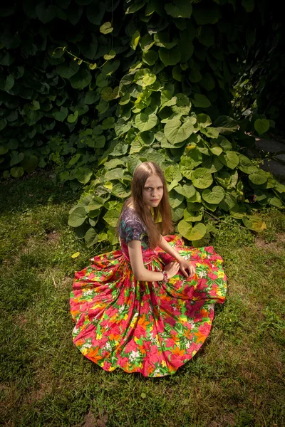 Mujer en falda de colores sentado en la hierba junto a los arbustos — Foto de Stock