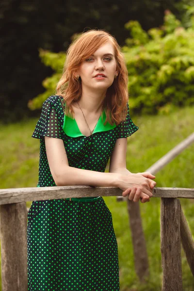 Portrait of redhead woman in green dress on wooden bridge — Stock Photo, Image