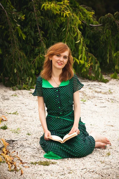 Redhead woman in green dress reading book at garden — Stock Photo, Image