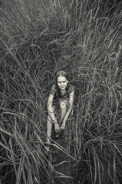 Foto monocromática de una chica solitaria sentada en el césped en el campo —  Fotos de Stock