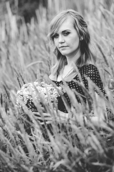 Monochrome portrait of woman holding bunch of flowers at field — Stock Photo, Image