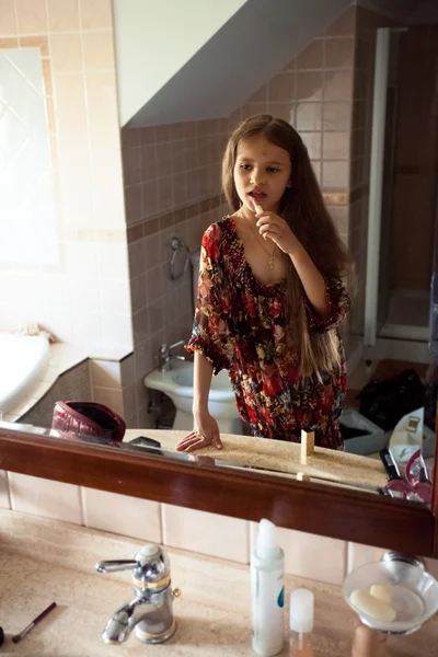 Cute girl looking at mirror and painting lips with red lipstick — Stock Photo, Image