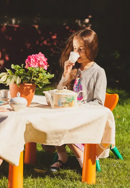 Cute girl drinking tea at toy table at yard — Stock Photo, Image