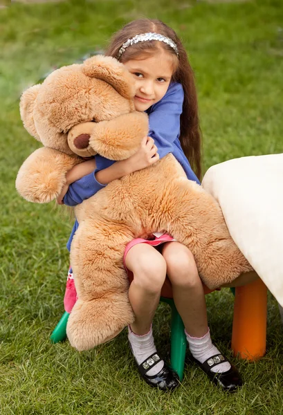 Mädchen umarmt großen Teddybär, während sie auf Stuhl im Hof sitzt — Stockfoto