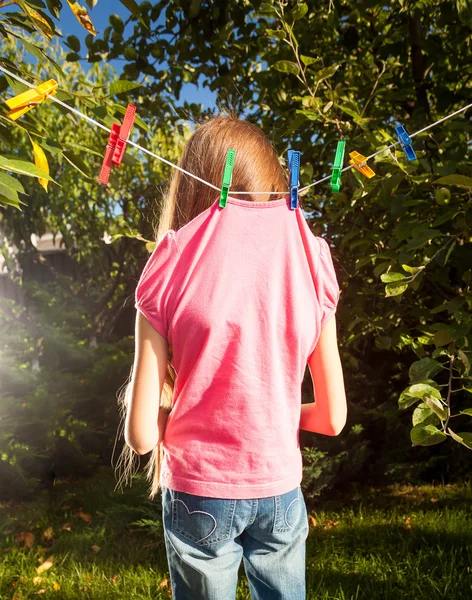 Little girl hanged by clothespins on rope — Stock Photo, Image