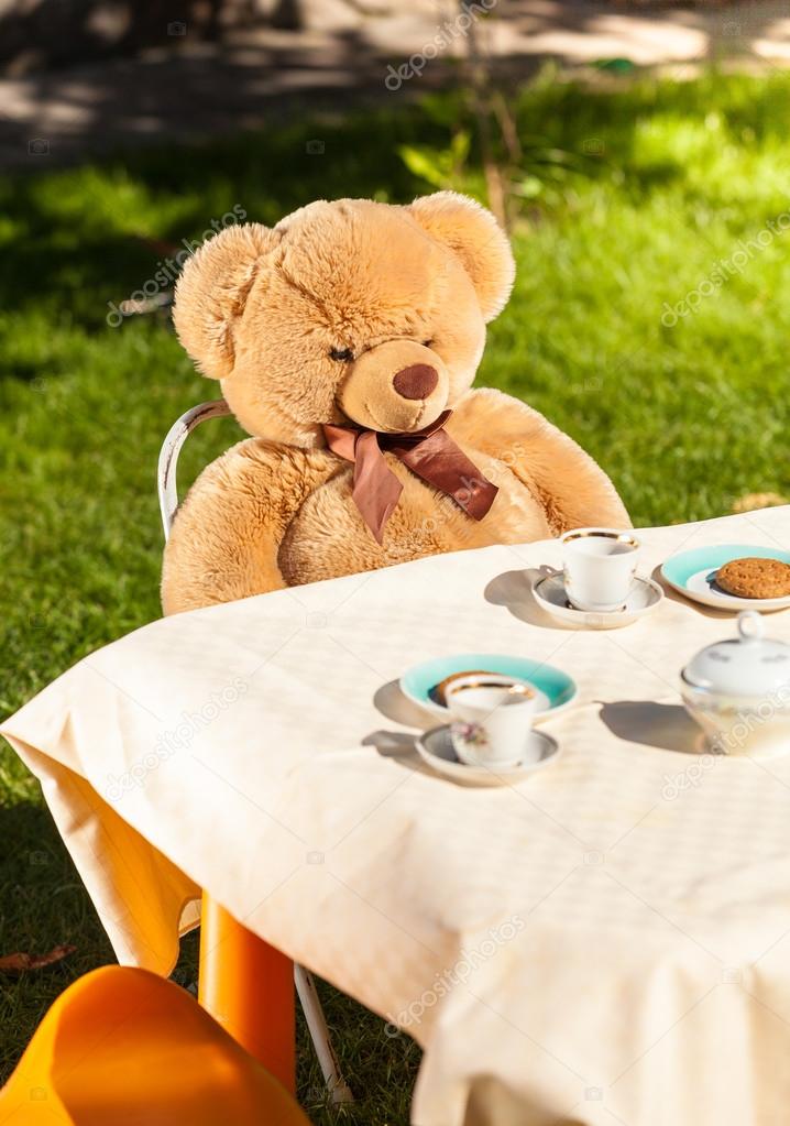 teddy bear sitting behind table and drinking tea
