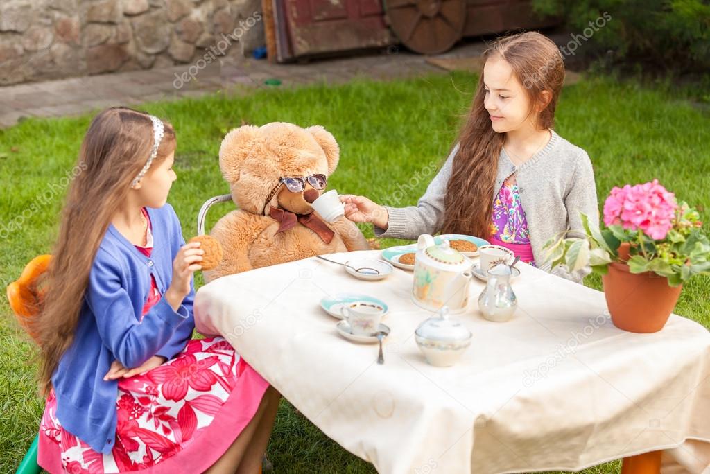 girls having tea party with teddy bear at yard