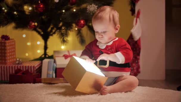 Lindo bebé con traje de Santa mirando dentro de la caja de regalo de Navidad. Familias y niños celebrando las vacaciones de invierno. — Vídeos de Stock