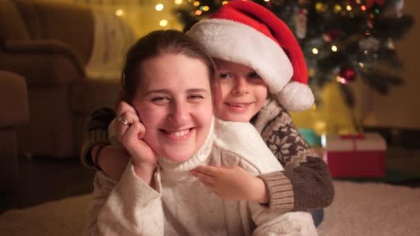 Porträtt av leende mor med son i tomte hatt liggande på golvet på julafton. Rena känslor hos familjer och barn som firar vinterlov. — Stockvideo