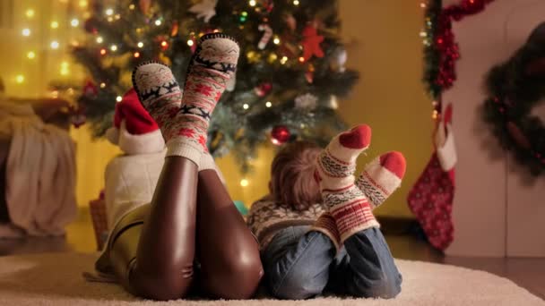 Zbliżenie stóp rodziny w dzianiny wełniane skarpetki leżące obok świecącej choinki w salonie. Czyste emocje rodzin i dzieci świętujących zimowe wakacje. — Wideo stockowe