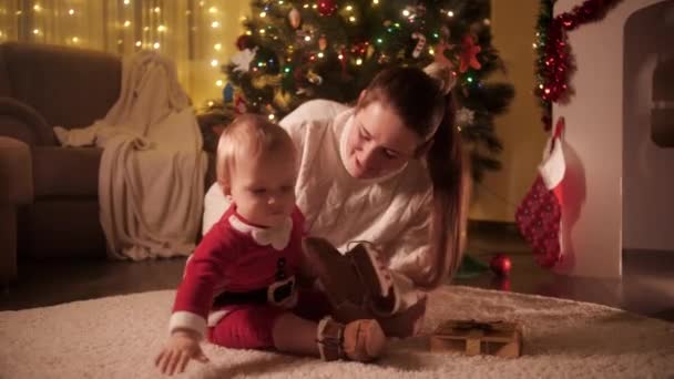 Aranyos kisfiú télapó jelmezben mászkál a padlón a karácsonyfa alatt. A téli ünnepeket ünneplő családok és gyermekek. — Stock videók