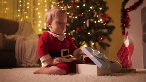 Το αγοράκι με τη στολή του Αϊ Βασίλη ανοίγει το κουτί των Χριστουγέννων. Οικογένειες και παιδιά γιορτάζουν χειμερινές διακοπές. — Αρχείο Βίντεο