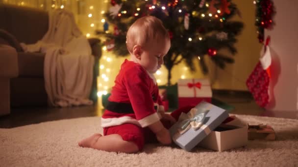 Aranyos baba játszik karácsonyi ajándék doboz alatt díszített karácsonyfa. A téli ünnepeket ünneplő családok és gyermekek. — Stock videók