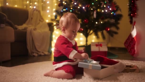 Маленький мальчик открывает рождественскую подарочную коробку и заглядывает внутрь. Семьи и дети празднуют зимние праздники. — стоковое видео