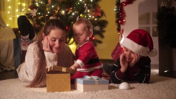 Retrato de un bebé sonriente con su hermano y su madre tumbados en el suelo en Navidad. Familias y niños celebrando las vacaciones de invierno. — Vídeos de Stock