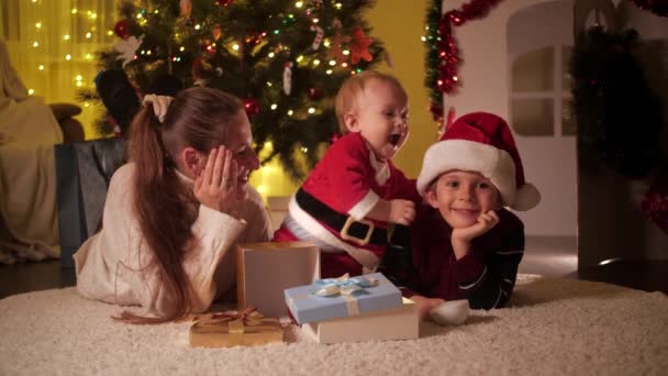 Noel arifesinde tatlı erkek bebek anne ve erkek kardeşle oynuyor. Aileler ve çocuklar kış tatilini kutluyor. — Stok video