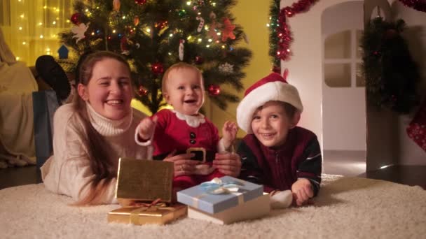행복 한 엄마와 아이들 이 집에 있는 크리스마스 트리 밑 바닥에 누워 있는 모습. 겨울철 휴일을 기념하는 가족 과 자녀들. — 비디오