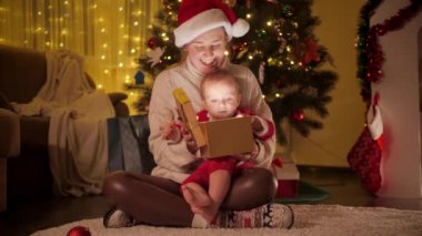 Mutlu gülen anne ve küçük oğlu Noel hediyesi kutusunu tutuyor ve kameraya gülümsüyor. Aileler ve çocuklar kış tatilini kutluyor.