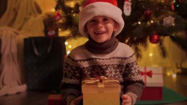 Noel hediyesini tutan ve hediye kutusuna bakan neşeli çocuk portresi. Aileler ve çocuklar kış tatilini kutluyor.