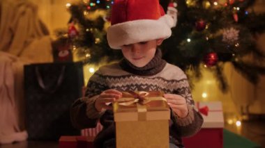 Noel Baba şapkalı heyecanlı çocuğun portresi hediye kutusuna bakıyor. Aileler ve çocuklar kış tatilini kutluyor.