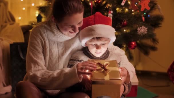 Een gelukkige moeder met een zoon die in een magische kerstdoos kijkt. Gezinnen en kinderen vieren wintervakantie. — Stockvideo