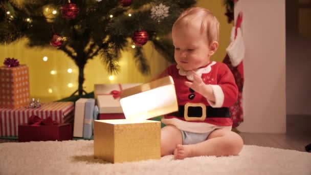 Lindo niño desenvolviendo y mirando dentro de la caja de regalo de Navidad bajo el árbol de Navidad decorado. Familias y niños celebrando las vacaciones de invierno. — Vídeos de Stock